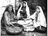 Village women, seated outside their houses, grinding corn. An early photograph.